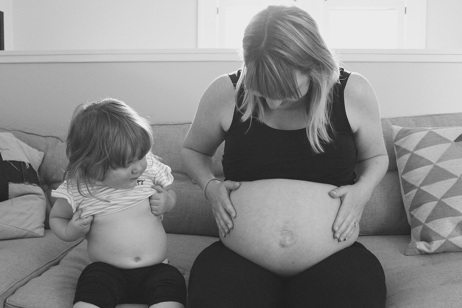 A woman shows her pregnant belly to her toddler in an example of pregnancy photo ideas.