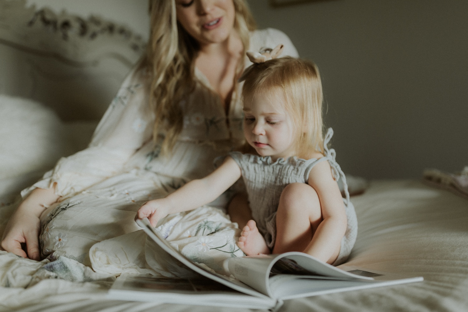 A mother sits beside a child flipping through a keepsake book on her bed.