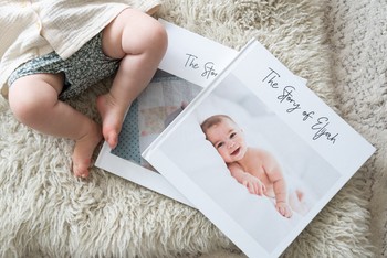 A baby lays on a rug next to photo albums with different memory book title ideas.