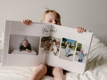 A toddler holds open a memory book journal showing toddler milestones.