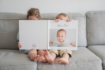 Two children sit side by side reading a toddler memory book.