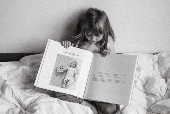 A toddler holding her modern baby book open to the 2-month-old baby book page